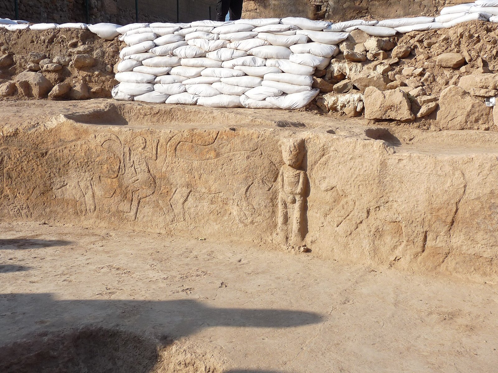 The Sayburç relief-bearing bench in situ during excavation, carved figures visible along the bench with protective sandbags behind