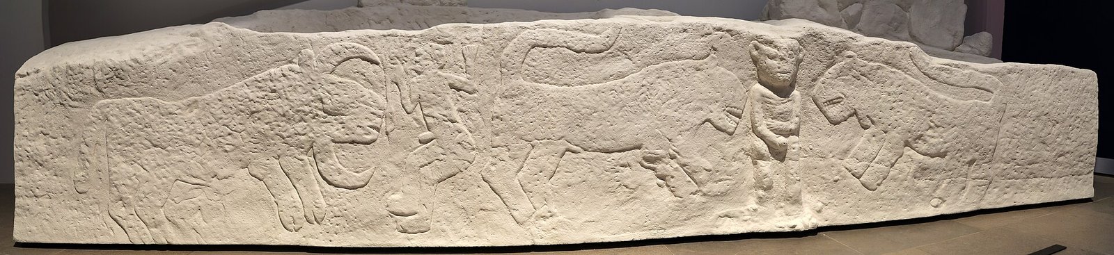 Photograph of the Sayburç bench relief: two leopards, two human figures and a bull carved along a stone bench