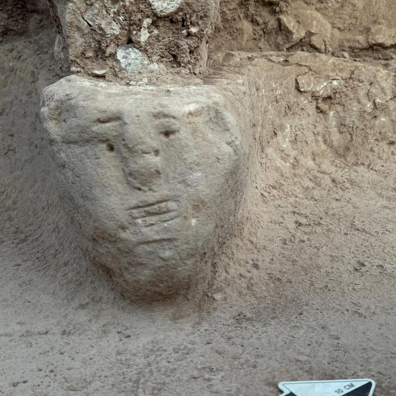 A human face carved into the bedrock base of a standing pillar at Sayburç, with a 10 cm scale marker beside it