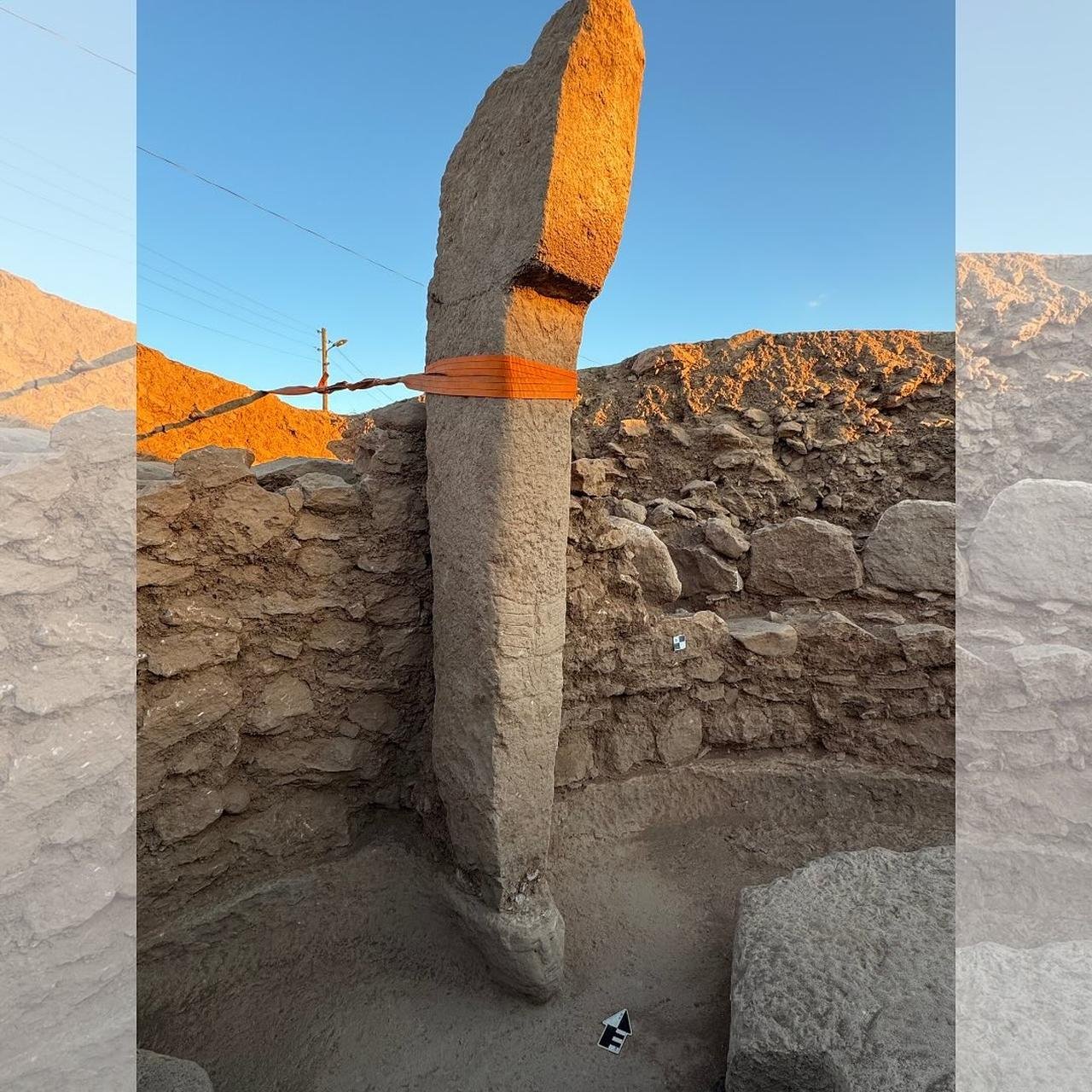 A tall standing pillar at Sayburç, strapped for preservation, rising inside a stone-walled building opposite a niche